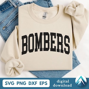 Op de afbeelding: Een crèmekleurige sweatshirt met het woord "BOMBERS" in vette, zwarte blokletters over de voorkant. De sweatshirt is over een spijkerbroek gevouwen. De onderkant van de afbeelding bevat de tekst "SVG PNG DXF EPS" en "digitale download".