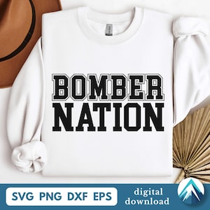 Op de afbeelding: Een witte sweatshirt met de tekst "BOMBER NATION" in dikke, zwarte blokletters. Daaronder de bestandstypen: SVG, PNG, DXF en EPS. De woorden "digitale download" zijn ook aanwezig.