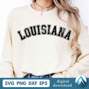 Puede incluir: Una sudadera de manga larga de color crema con la palabra LOUISIANA impresa en una fuente universitaria negra, audaz y arqueada en el pecho. La prenda tiene un cuello redondo y mangas largas, ofreciendo una estética sencilla y limpia.