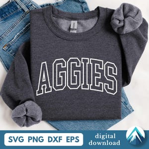 Op de afbeelding: Een donkergrijs sweatshirt met het woord "AGGIES" in witte blokletters. Het sweatshirt is opgevouwen op een blauwe spijkerbroek. De mouwen zijn opgerold. De onderkant van de afbeelding bevat de woorden "SVG PNG DXF EPS" en "digitale download".