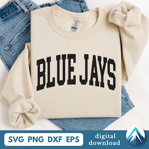 Op de afbeelding: Crèmekleurige sweatshirt met de tekst "BLUE JAYS" in vette, zwarte letters. De sweatshirt is opgevouwen op een blauwe spijkerbroek. De afbeelding bevat ook de tekst "SVG PNG DXF EPS" en "digitale download".