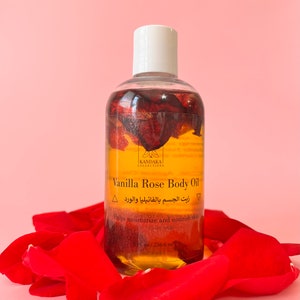 Puede incluir: Una botella de vidrio transparente de aceite corporal de vainilla y rosa con una tapa blanca, rodeada de p&eacute;talos de rosa rojos. La botella contiene un l&iacute;quido dorado con p&eacute;talos de rosa en su interior. El texto en la botella dice "Vanilla Rose Body Oil" y "236,6 ml".