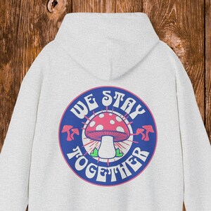 May include: White hooded sweatshirt with a blue circle graphic featuring a mushroom with red and white spots and the text "We Stay Together".
