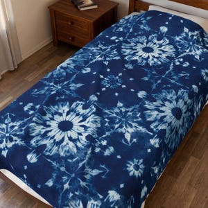 May include: A dark blue and white tie-dye blanket featuring a repeating pattern of large, intricate floral-like mandala shapes. The fabric displays a deep indigo background with lighter blue and white circular motifs spread across the entire surface.