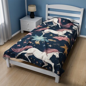 May include: A navy blue twin-sized bedspread with a whimsical design featuring white unicorns with pink manes and tails galloping across a starry night sky. The stars are gold and blue, and there are also pink clouds.