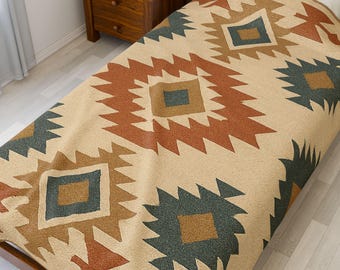 May include: A beige blanket with a geometric pattern in shades of brown, rust, and teal. The design features diamond shapes with a southwestern or tribal aesthetic. The blanket is on a wooden bed frame.