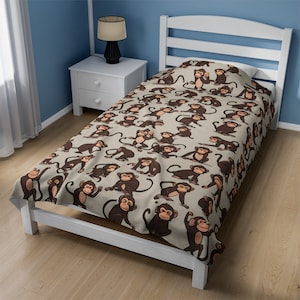 May include: A beige twin-sized bedspread with a repeating pattern of brown monkeys in various poses. The bedspread is on a white bed frame with a wooden headboard.