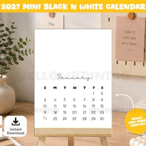 May include: A 2027 mini black and white calendar on a wooden easel stand. The calendar page displays the month of January with a grid of dates in black text on a white background. The calendar is positioned upright, showing the days of the week.
