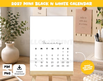 May include: A 2027 mini black and white calendar on a wooden easel stand. The calendar page displays the month of January with a grid of dates in black text on a white background. The calendar is positioned upright, showing the days of the week.