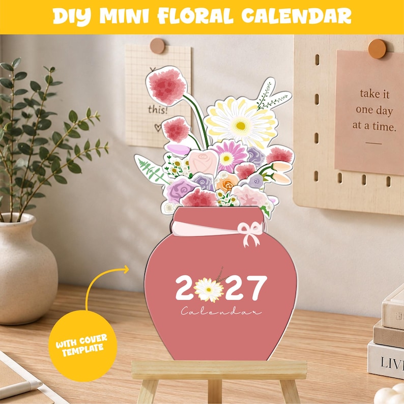 May include: A DIY mini floral calendar featuring a pink vase-shaped base with the text 2027 Calendar and a white flower graphic. The top displays a colorful illustration of various flowers including pink, yellow, and white blossoms with green leaves.
