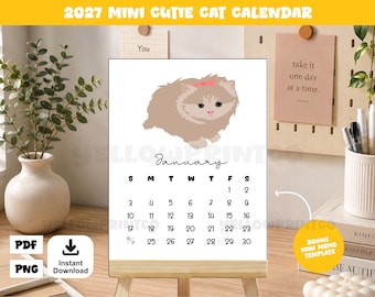 May include: A 2027 mini calendar featuring a light brown fluffy cat illustration with a pink bow on its head. The page displays the month of January with black text and numbers on a white background, set on a small wooden easel stand.