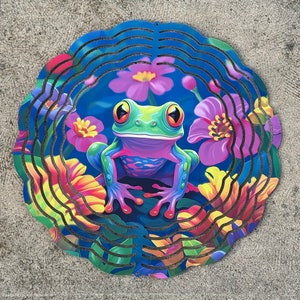 May include: A colorful metal wind spinner featuring a green frog with pink and blue accents surrounded by flowers. The frog is sitting on a blue background with yellow, orange, pink, and purple flowers.