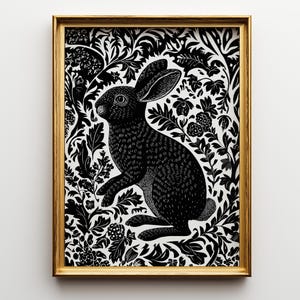 May include: A framed wall art print featuring a black and white illustration of a rabbit surrounded by dense, intricate foliage and floral patterns. The artwork is enclosed in a thin, metallic gold rectangular frame with a clean, sharp finish.