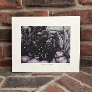 May include: Black and white art print titled "Greyhounds on Parade" featuring a detailed illustration of greyhounds in a natural setting with ferns and other plants. The print has a white border and is displayed against a brick wall.