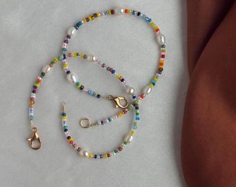May include: A colourful beaded necklace with white pearls and gold clasps. The necklace is made of small, colourful beads and has a delicate, feminine look.