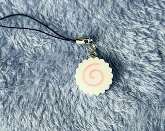 Peut inclure: Un charm narutomaki blanc et rose avec un fermoir argenté et un cordon noir. Le charm présente un motif en spirale et se détache sur un fond bleu texturé.