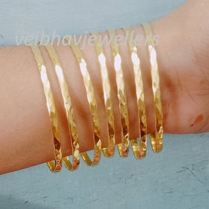 Könnte beinhalten: Gehämmerte Armreifen in Gold. Die Armbänder haben eine strukturierte Oberfläche und werden am Handgelenk getragen. Der Schmuck wird vor einem hellblauen Hintergrund präsentiert. Der Text "veibhavjewellers" ist sichtbar.