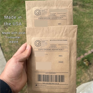May include: A brown paper envelope with a USPS Ground Advantage label. The label has the text "USPS Ground Advantage" and a tracking number. The envelope also has the text "100% Recyclable Packaging" and "Made in the USA". The envelope is being held by a hand. The text "Order Today!" is printed on the bottom of the envelope.