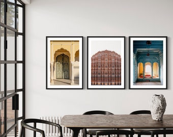 May include: Three framed photographs of architectural details in India. The first photo shows a yellow building with a green door and archway. The second photo shows a pink building with many windows and arches. The third photo shows a blue building with a large archway and a red rug.