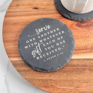 May include: Round, gray slate coaster with the text "...serve ONE ANOTHER WITH, WHATEVER EACH OF YOU HAS RECEIVED." 1 PETER 4:10" in white. A white mug sits on a matching coaster, on a wooden tray.