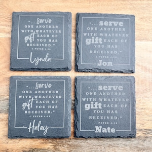 May include: Four square dark gray slate coasters with rough, natural edges. Each coaster is engraved with the text: '...serve one another with whatever gift each of you has received.' followed by '1 Peter 4:10' and the names Lynda, Jon, Haley, or Nate.