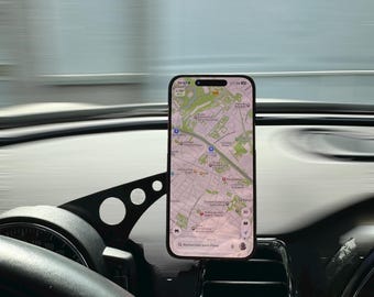 Peut inclure: Un smartphone affiche une application de cartographie, monté sur le tableau de bord d'une voiture. Le téléphone est maintenu par un support noir, près de la grille d'aération. Le volant et le tableau de bord sont visibles, avec un arrière-plan flou.