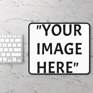 May include: White rectangular mousepad with black trim and the text "YOUR IMAGE HERE" in bold black letters. A silver keyboard is partially visible on a marble surface.