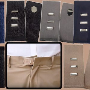 May include: A collection of adjustable waist extenders for trousers, featuring various fabric colors including navy, black, gray, and beige. Some extenders use gold-toned buttons with leaf motifs, while others utilize silver-toned metal hooks and bars.