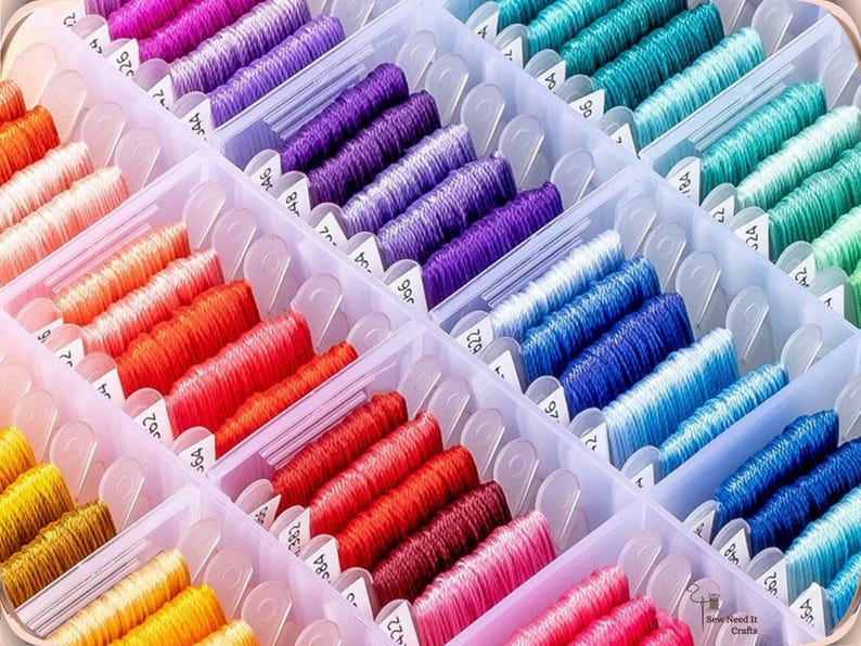 May include: A clear plastic organiser filled with spools of colourful embroidery floss. The floss is arranged by colour, including shades of pink, red, orange, yellow, purple, blue, and green. Each spool is labelled with a number. The image is well-lit and shows the variety of colours.