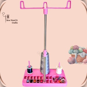 Pode incluir: Suporte de fio de costura rosa com uma haste de metal, dois porta-bobinas e um compartimento para bobinas e outros suprimentos de costura. O suporte tem uma barra superior para segurar o fio.