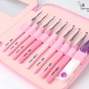 May include: A set of pink crochet hooks in a pink case. The set contains eight crochet hooks, ranging in size from 2.5mm to 6.0mm, and a purple accessory. The case is open, displaying the hooks in an organised manner.