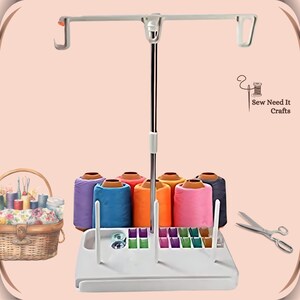 Pode incluir: Suporte de fio de costura de pl&aacute;stico branco com uma haste e ganchos de metal. O suporte tem seis rolos de fio de v&aacute;rias cores, um compartimento para bobinas e um pequeno compartimento para outros suprimentos de costura. O suporte &eacute; etiquetado como "Sew Need It Crafts".