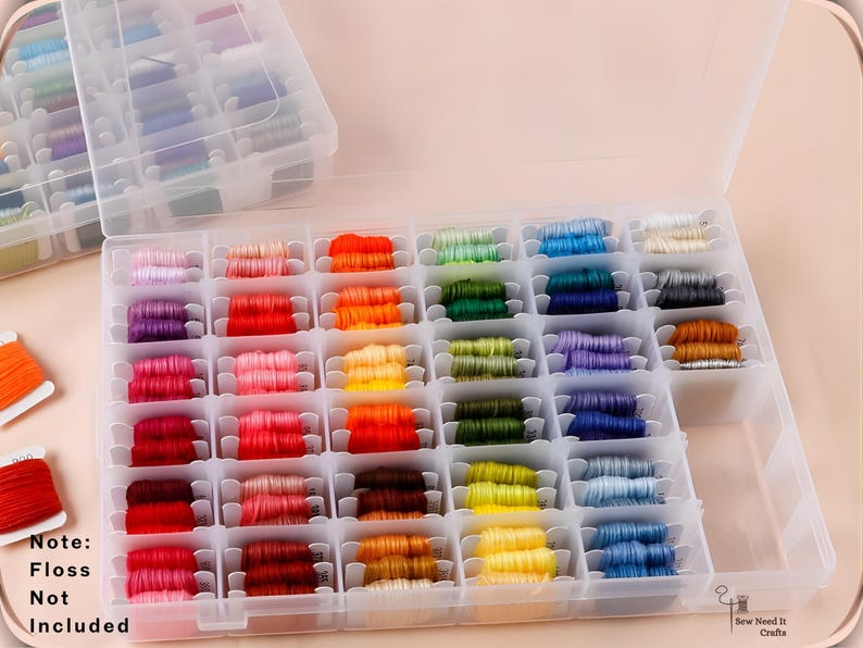 May include: A clear plastic storage box filled with colourful embroidery floss. The floss is arranged in a grid of small compartments, showcasing a spectrum of colours from pinks and reds to blues and greens. The text "Note: Floss Not Included" is visible.