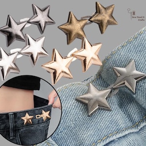 Puede incluir: Tachuelas metálicas en forma de estrella en acabados plateado, dorado y bronce. Las tachuelas se muestran sobre tela vaquera, lo que sugiere su uso como adornos decorativos para ropa o accesorios.