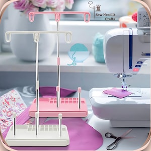 Pode incluir: Um organizador de linha de costura branco e rosa com um suporte e duas barras para pendurar carret&eacute;is. O organizador tem um compartimento para guardar carret&eacute;is e agulhas. O organizador est&aacute; sentado em uma mesa ao lado de uma m&aacute;quina de costura.
