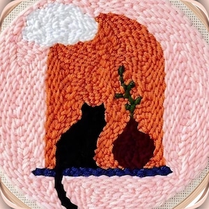 May include: A pink and orange needlepoint hoop art piece with a black cat silhouette, a brown vase with green leaves, and a white cloud.