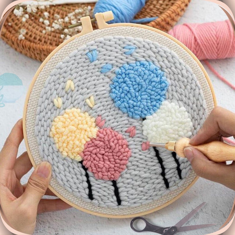 May include: A close-up of a gray embroidery hoop with a colorful yarn design of four flowers. The flowers are pink, yellow, white, and blue. A wooden needle tool is being used to create the design.