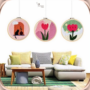 May include: Three embroidery hoop wall art pieces with a pink, green, and white background. The pink hoop features a pink flower with green leaves, the green hoop features a red flower with green leaves, and the white hoop features a black cat and a vase with a flower.