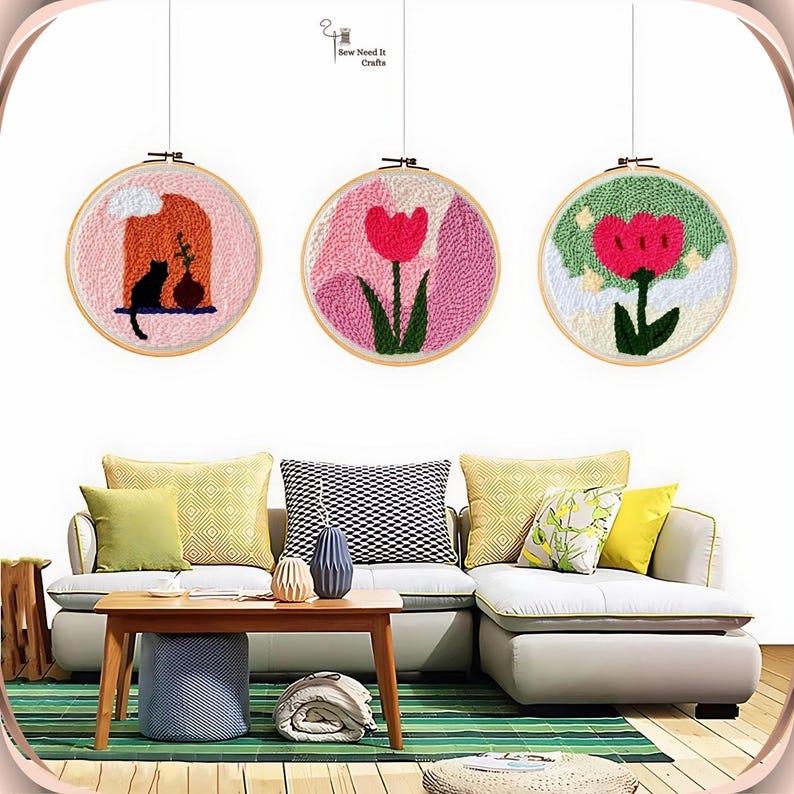 May include: Three embroidery hoop wall art pieces with a pink, green, and white background. The pink hoop features a pink flower with green leaves, the green hoop features a red flower with green leaves, and the white hoop features a black cat and a vase with a flower.