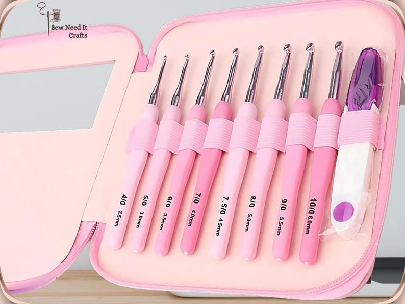 May include: A pink crochet hook set in a zippered case. The set includes nine crochet hooks in varying shades of pink, with sizes ranging from 2.5mm to 6.0mm. The case is open, revealing the hooks neatly arranged in individual slots. The text "Sew Need It Crafts" is visible.