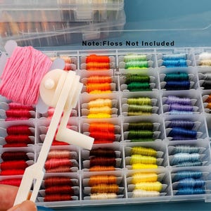 May include: A clear plastic storage box containing a selection of colourful embroidery threads. The threads are arranged in a variety of shades, including pink, red, orange, yellow, green, blue, and purple. A white thread winder is in the foreground. Text in the image reads "Note: Floss Not Included".