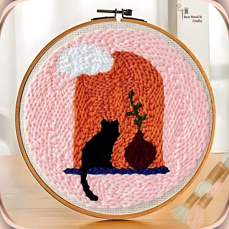 May include: A pink and orange wool punch needle embroidery hoop with a black cat silhouette, a green plant, and a brown vase. The embroidery is set against a white cloud in a pink sky.