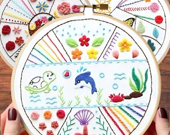 May include: A white embroidery hoop with a colorful design of a turtle, dolphin, seashells, and starfish. The design is surrounded by a rainbow of colors.