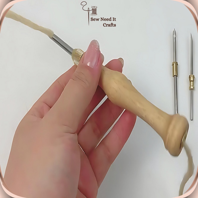 May include: A wooden needle threader with a brass tip and a long, thin needle. The threader is being held in a hand, and a length of white thread is coming out of the needle. The text "Sew Need It Crafts" is visible in the top right corner of the image.