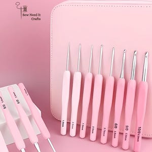 May include: A collection of pink crochet hooks with silver metal tips, displayed in front of a matching pink case. The hooks are labelled with sizes, ranging from 0.5mm to 6.0mm. The image includes the text "Sew Need It Crafts".