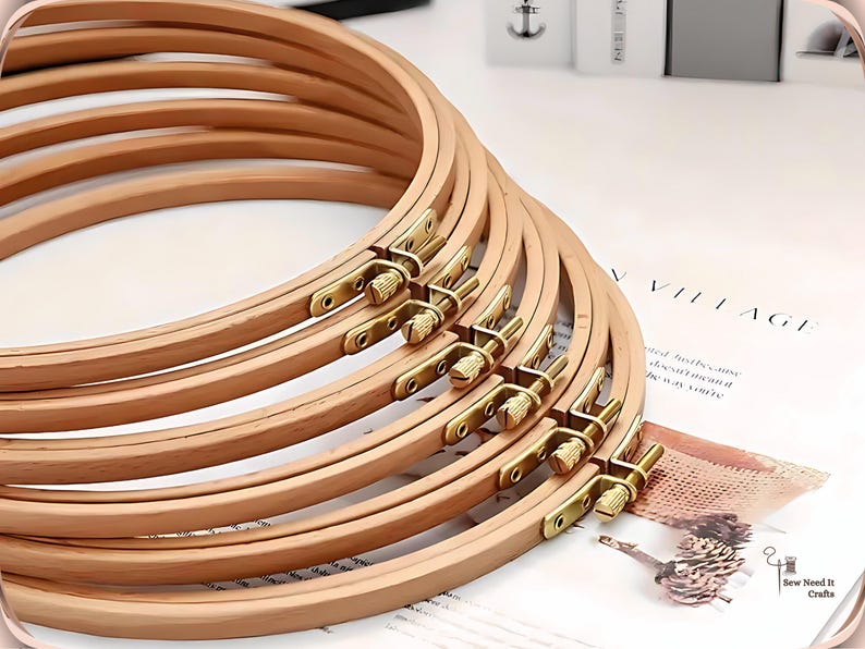 May include: A stack of wooden embroidery hoops with brass hardware. The hoops are light brown and arranged in a fan shape, with the brass fasteners visible. The background includes a printed page with the word "VILLAGE".