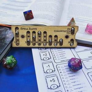 Puede incluir: Un rastreador de espacios de conjuro de madera rectangular con rodamientos de metal para seguir los niveles del uno al nueve, con el texto "Spell Slots" y "Concentration On/Off". El rastreador está rodeado de dados poliédricos.