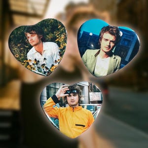 May include: Three heart-shaped buttons featuring images of a man in different settings. One button shows the man in a white shirt, another in a green jacket, and the third in a yellow jacket.