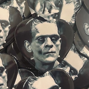 May include: A collection of heart-shaped pin-back buttons featuring a black and white portrait of Frankenstein's monster. Each button displays the iconic character with a flat-top hairstyle, heavy brow, and neck bolts, rendered in high-contrast grayscale.