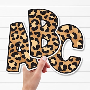 May include: Three individual die-cut letters A, B, and C featuring a tan and black leopard print pattern. Each letter has a thick white border outline, creating a distinct sticker-like appearance for these alphabet characters.